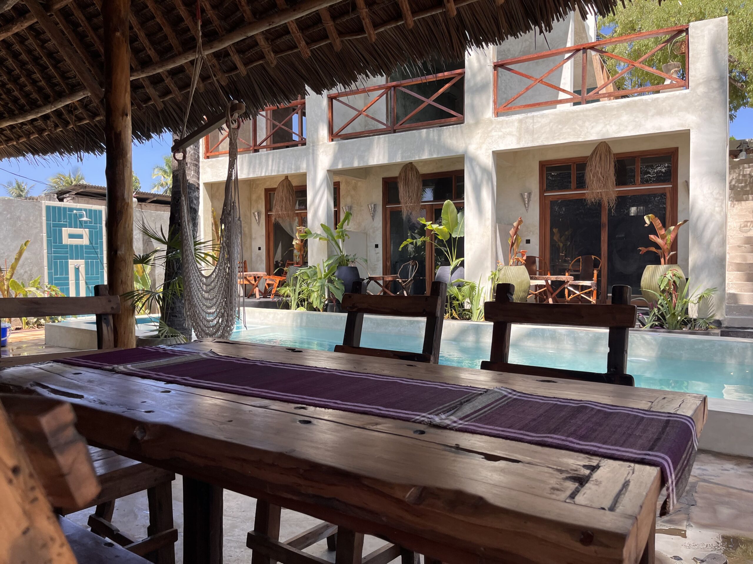 View from a wooden dining table across the courtyard pool at a Zanzibar bungalow.