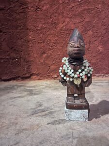 Carved wooden statue with beaded necklaces against a textured red wall in Zanzibar.