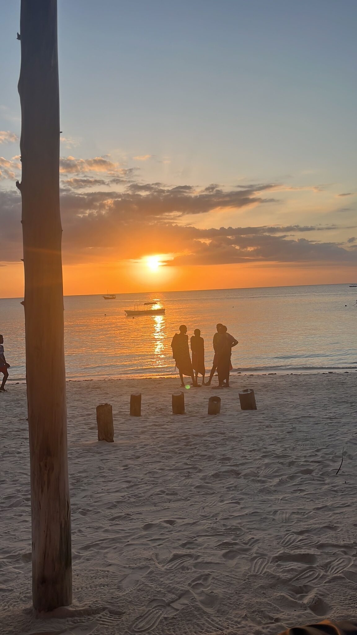Sunset over the Indian Ocean on a Zanzibar beach with silhouettes of people by the water.
