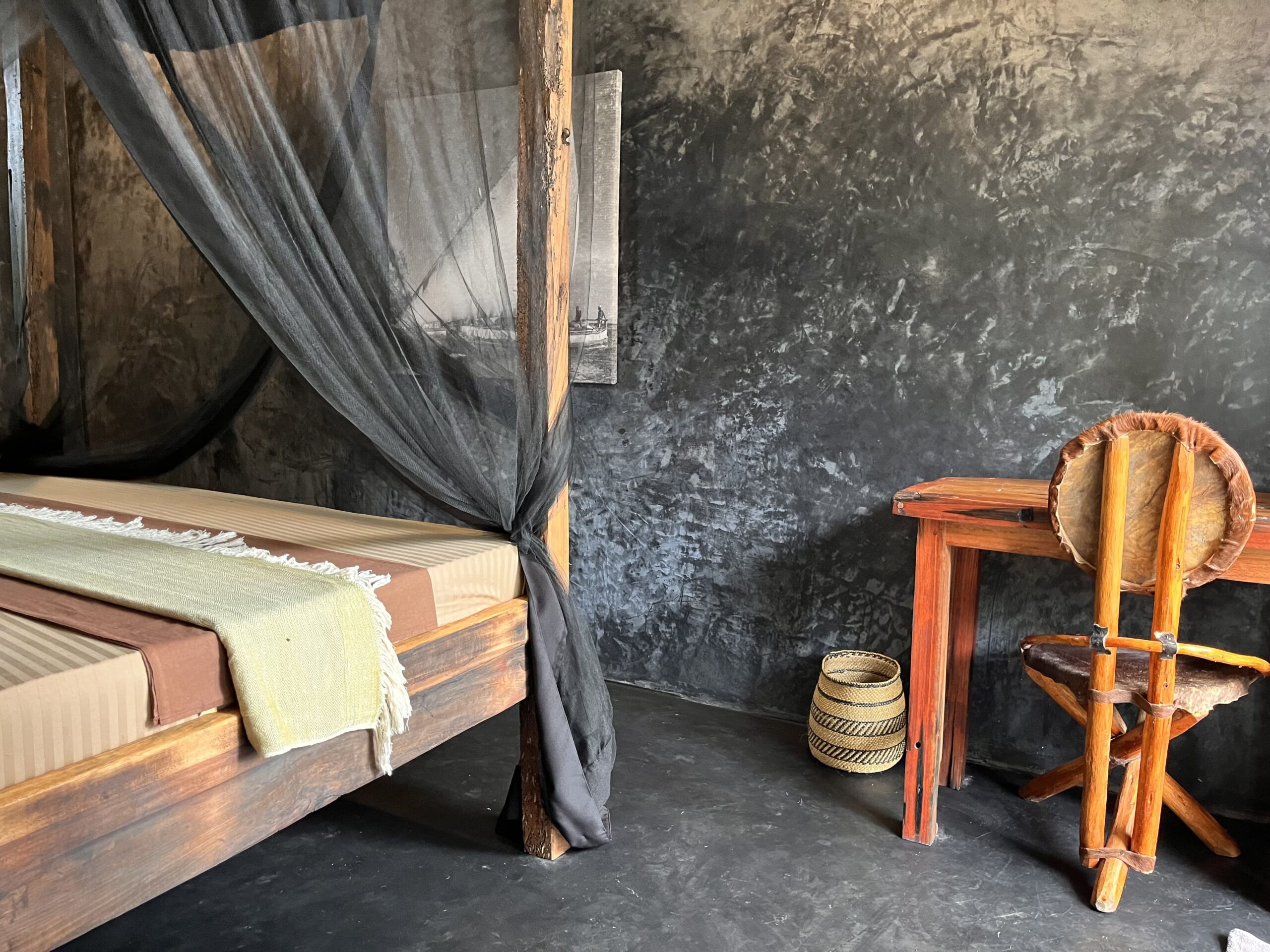 Cozy bungalow bedroom in Zanzibar with wooden bed, mosquito net and rustic desk.