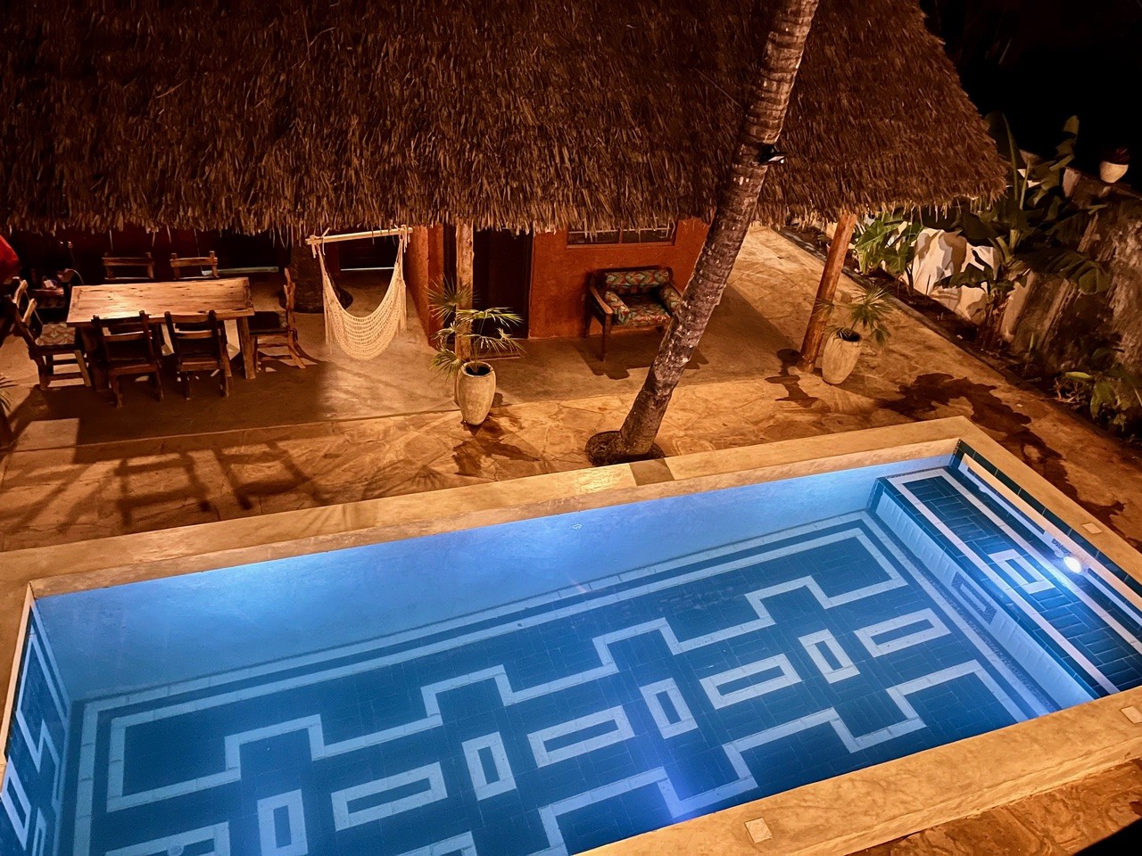 Zanzibar bungalow courtyard with lit swimming pool and covered outdoor dining area at night.