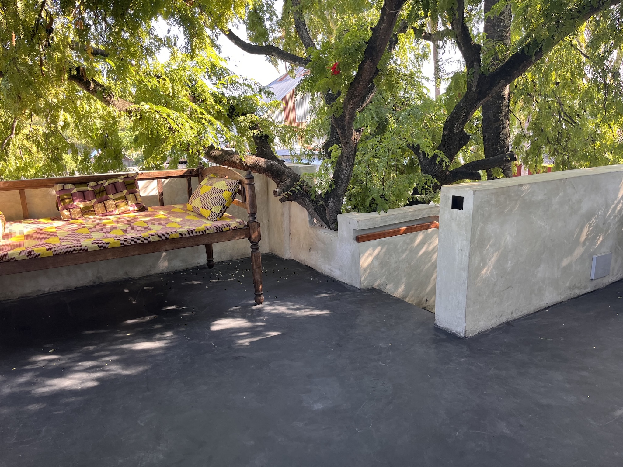 Rooftop terrace with wooden daybed under a large tropical tree in Zanzibar.