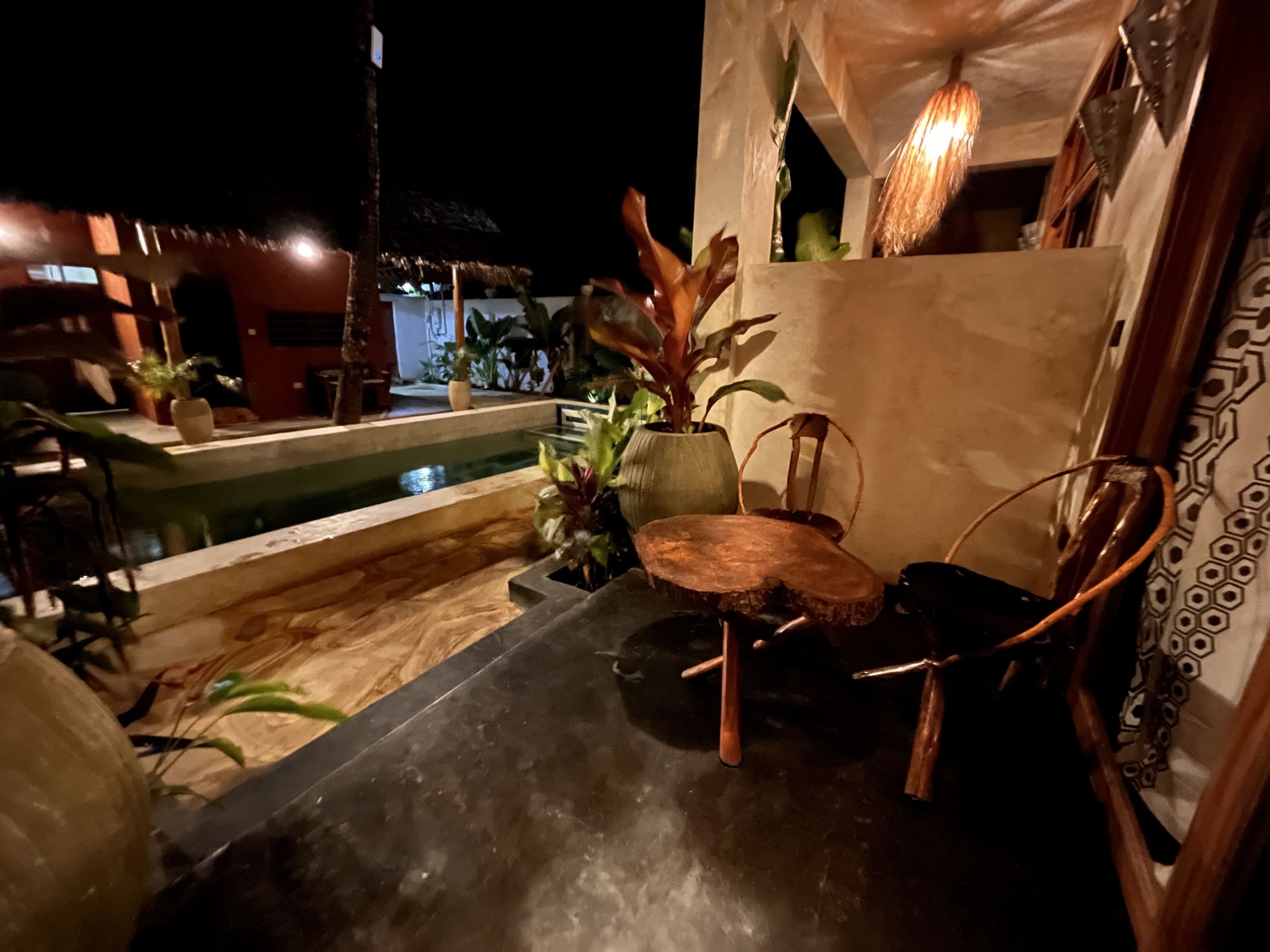 Cozy terrace seating area overlooking a private pool at night in a Zanzibar bungalow.