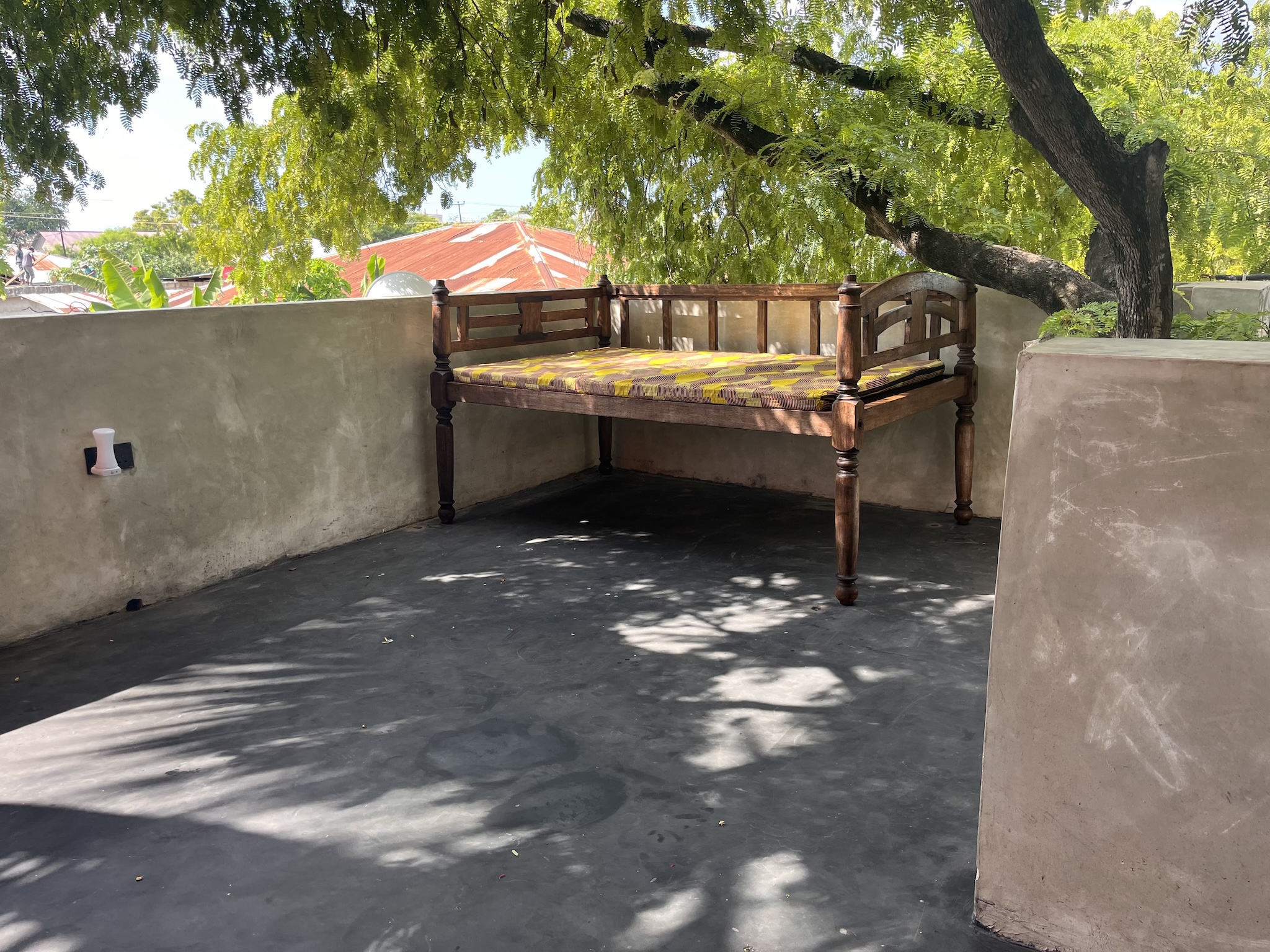 Close view of wooden daybed on shaded rooftop terrace in Zanzibar bungalow.